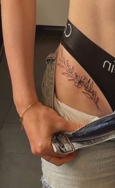 a woman with a tattoo on her stomach holding onto a pair of jeans and looking at the camera