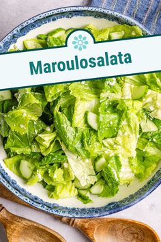 a bowl filled with lettuce and cucumbers next to wooden spoons