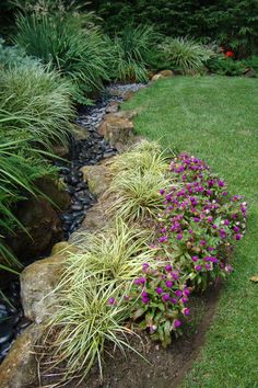 a garden filled with lots of different types of flowers and plants next to a lush green lawn