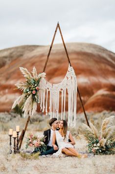 a man and woman sitting on the ground in front of a teepee with flowers