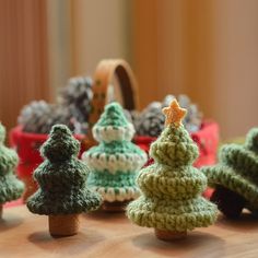 small knitted christmas trees sitting on top of a wooden table next to pine cones