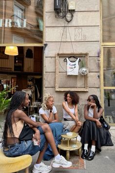 four women sitting on the sidewalk in front of a building talking to eachother