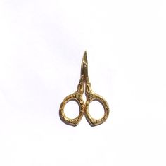 a pair of gold colored scissors sitting on top of a white surface with no background