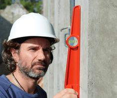 a man wearing a white hard hat and holding a red piece of equipment in his hand