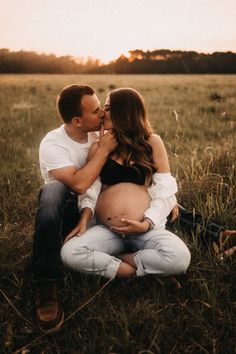 a pregnant couple kissing while sitting in the grass