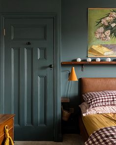 a bedroom with green walls and a painting on the wall above the bed, next to a brown leather headboard