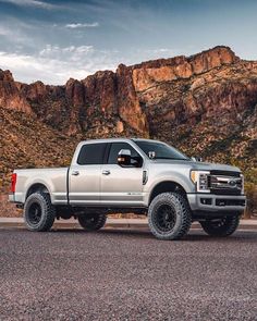 a silver truck is parked on the side of the road in front of some mountains