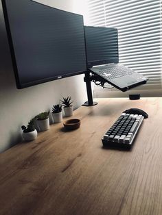 a desk with a keyboard, monitor and plant on it in front of a window