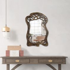 an ornate mirror hangs on the wall above a wooden table with two drawers and a lamp