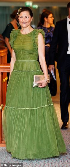 a woman in a green dress is walking down the hall with other people behind her