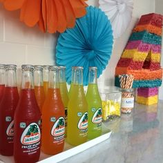 there are many drinks on the shelf in the kitchen and one is orange, green, pink, blue