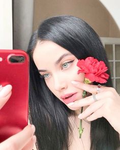 a woman with long black hair holding a red cell phone in front of her face