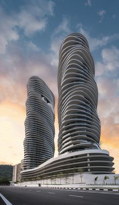 two very tall buildings sitting next to each other on the side of a road in front of a cloudy sky