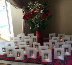 a table topped with pictures and candles next to a vase filled with red roses on top of a checkered table cloth