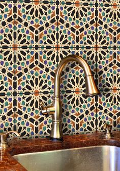 a kitchen sink under a faucet next to a wall with colorful tiles on it