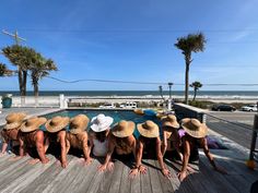 a group of women in hats sitting on top of a wooden deck next to a swimming pool