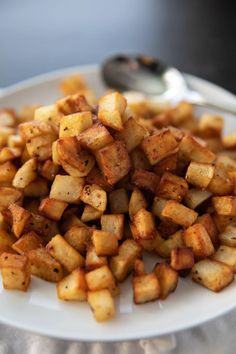 a white plate topped with fried potatoes on top of a table next to a spoon