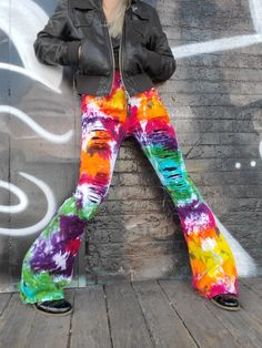 a woman standing in front of a graffiti wall wearing colorful pants and black leather jacket