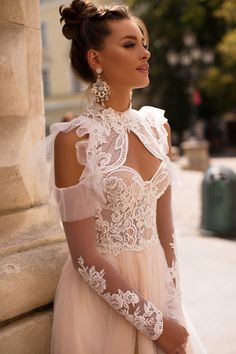 a woman in a white dress standing next to a stone wall and looking off into the distance