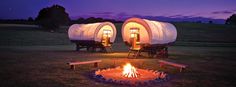 two white covered wagons sitting on top of a grass field next to a fire pit