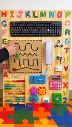 a child's hand is playing with a wooden toy keyboard and mouse set in front of a colorful puzzle board