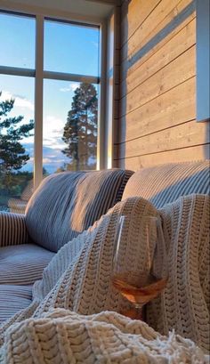 a glass of wine sitting on top of a bed in front of a large window