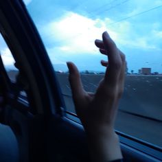 a person holding their hand out the window of a car on a highway at dusk