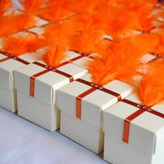 several boxes with orange feathers on them sitting next to each other in front of a white table cloth