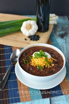 a white bowl filled with black bean soup and topped with sour cream, green onions and cheese