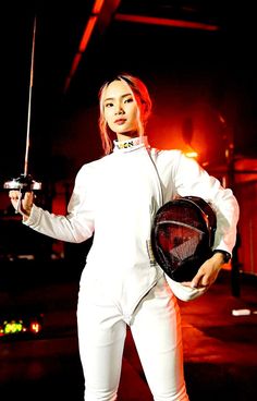 a woman in white is holding a tennis racket and wearing a fencing outfit while posing for the camera