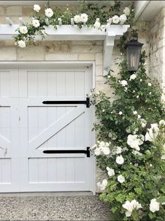 a white garage door surrounded by flowers and greenery