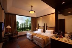 two beds in a hotel room with wooden flooring and large windows overlooking the trees