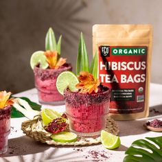 three cups filled with red tea and flowers next to a bag of organic hibiscus tea bags