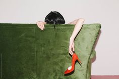 a woman is sitting on a green couch with her head resting on a high heeled shoe