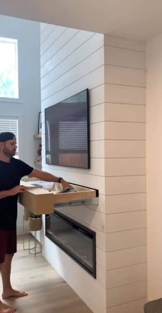 a man standing in front of a flat screen tv next to a wall mounted fireplace