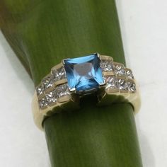 "This is a beautiful vintage ring! This stunning ring is made of 14k yellow gold. It is an elegant \"step\" style mounting with a 2 carat (approximate) square London blue topaz in the center. The topaz measures 6mm by 6mm and is set in a 4 prong head. On both sides of the topaz are 6 princess cut diamonds that step down in 3 steps, and graduate down in size from top to bottom. The princess cut diamonds are channel set. They are very white and sparkly, the diamonds are H-I in color and VS2-SI1 in Classic Princess Cut Topaz Ring With Diamond, Classic Asscher Cut Topaz Ring, Classic Diamond Topaz Ring With Princess Cut, Formal Princess Cut Blue Topaz Ring, Formal Princess Cut Topaz Ring With Center Stone, Classic Princess Cut Blue Topaz Ring, Classic Blue Topaz Princess Cut Ring, Classic Blue Topaz Ring With Princess Cut, Formal Princess Cut Topaz Ring