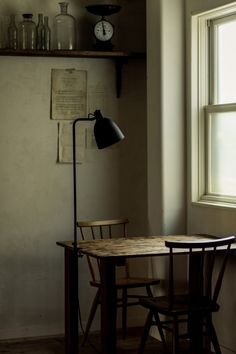 a table and chair in front of a window with a clock on the wall behind it