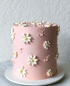 a pink frosted cake with white flowers on the top and bottom, sitting on a plate