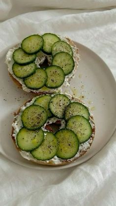 two pieces of bread with cucumbers on them sitting on a plate next to each other