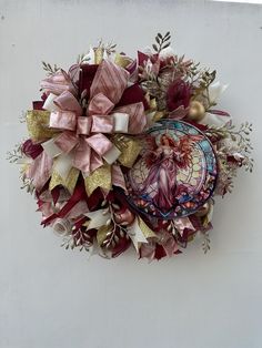 a wreath with an angel on it hanging from the side of a white wall next to a christmas ornament