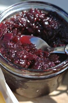 a glass jar filled with blueberry jam on top of a wooden table next to a spoon