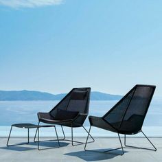 two brown chairs sitting next to each other on top of a cement floor with mountains in the background