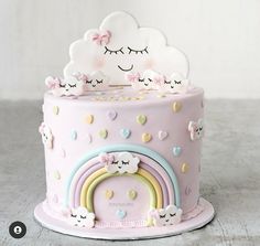 a pink cake decorated with clouds and rainbows