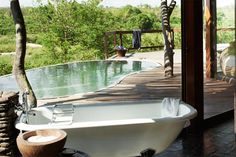 an outdoor bathroom with a large tub next to the pool and trees in the background