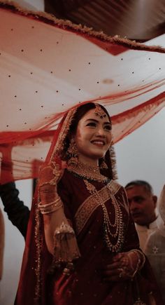 a woman in a red and gold bridal outfit smiles as she walks down the aisle