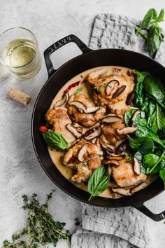 chicken with mushrooms and spinach in a skillet next to a glass of wine