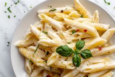 a white plate topped with pasta covered in sauce and basil leafy garnish