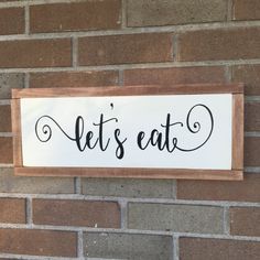 a wooden sign that says let's eat on the side of a brick wall