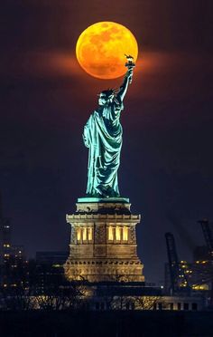 the statue of liberty lit up at night in new york city, with the full moon behind it