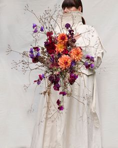 a woman holding a bouquet of flowers in front of her face and wearing a white dress